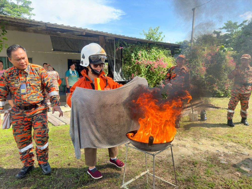 Salah seorang penduduk kampung mencuba memadamkan api dapur sambil ditunjuk ajar oleh pegawai bomba semalam. 