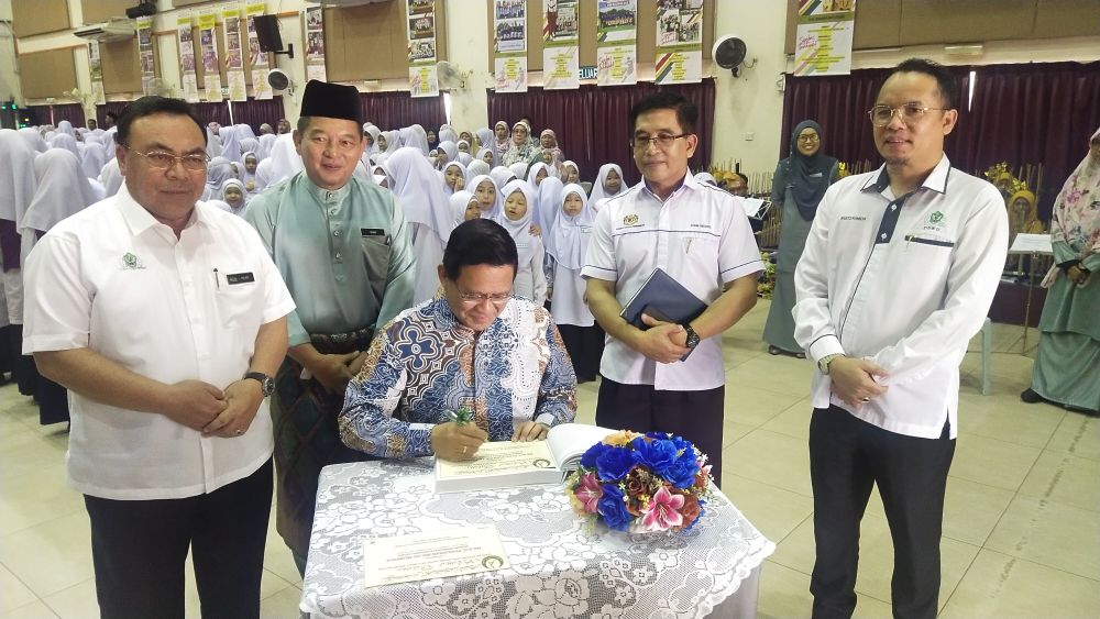 Dr Abdul Rahman menandatangani buku pelawat di SK (A) Datuk Haji Abdul Kadir Hassan, hari ini. Turut kelihatan Hilmy (kiri) serta yang lain.